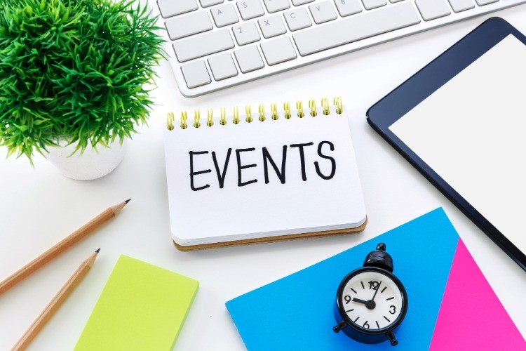 Image of a desktop containing a keyboard, watch, plant, pencils, paper, and a notebook with the word 'Events' written in bold font