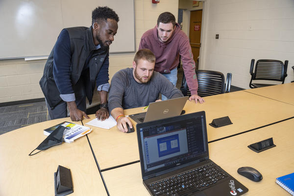 photo of three students looking at a laptop in a study room in the library
