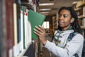 Student selecting book from library stacks