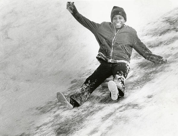 A young boy sledding down a snowy hill smiling