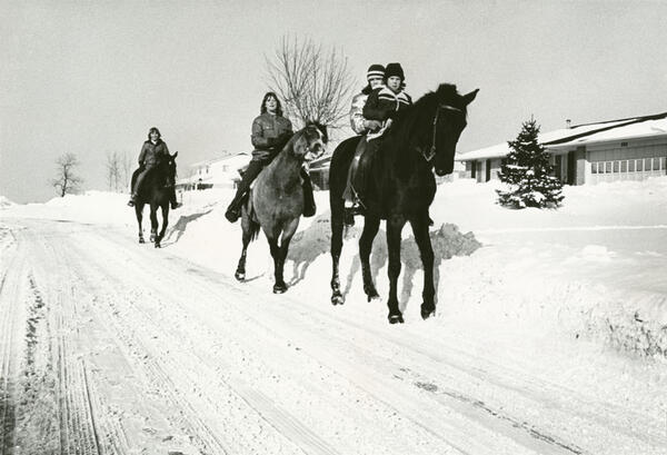 Four riders on three horses traveling on a snowy road