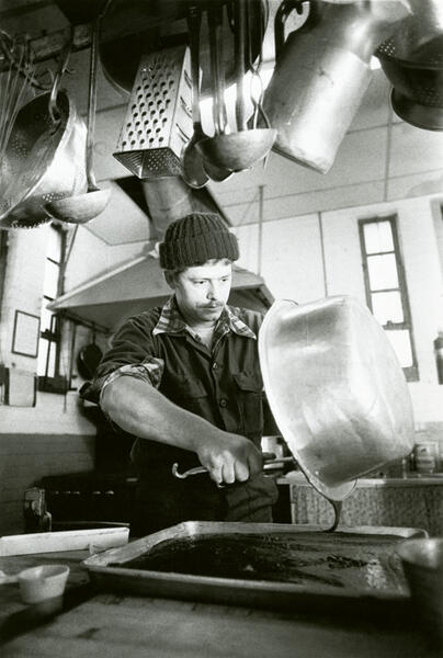 A man pouring brownie batter into a pan with kitchen utensils hanging above