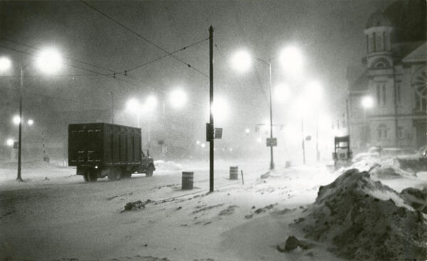 A snowy early morning scene with streetlights and a truck