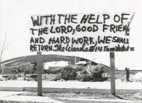 A sign that reads "with the help of the Lord, good friends, and hard work, we shall return. The Wards 814 Tomaha. The sign was near Warner Jr. High School (in the background), April 25, 1974..