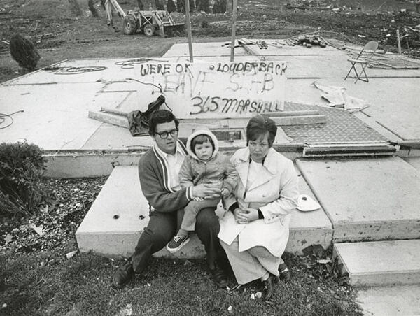 A couple with a young child sitting on the slab where their home had been.