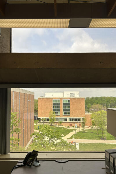 An indoor office window looking out towards an academic building