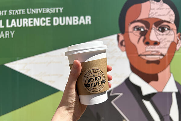 ReyRey Cafe coffee cup being held in front of the Paul Laurence Dunbar Library sign