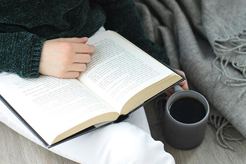 Person reading a book with a cup of coffee in hand