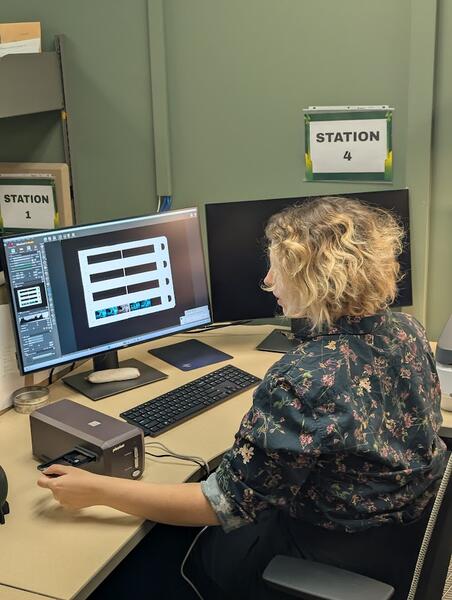 A person sitting at a computer with a negative scanner to their left.