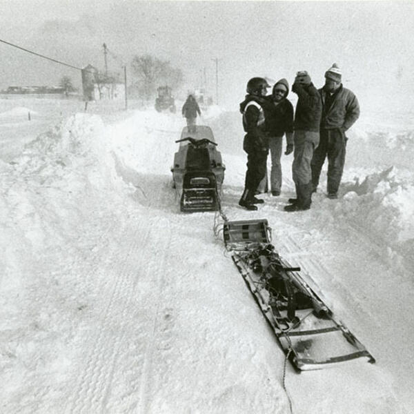 A group of four people talking by a snowmobile pulling a sled