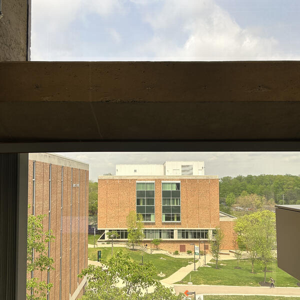 An indoor office window looking out towards an academic building