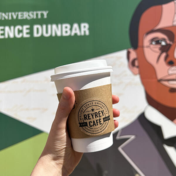 ReyRey Cafe coffee cup being held in front of the Paul Laurence Dunbar Library sign