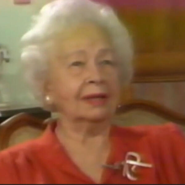 A woman in a red blouse talking to camera.