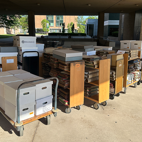 A row of 9 library carts filled with boxes lined up outside.