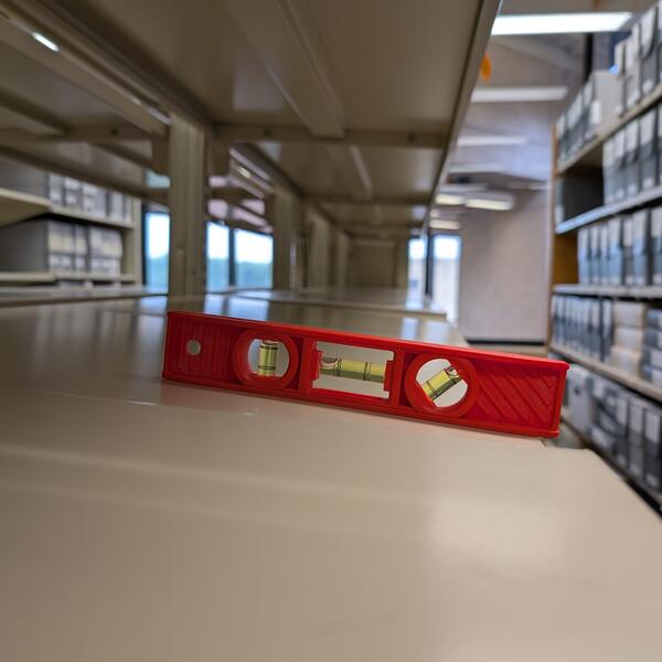 A level on an empty shelf. The level shows the shelf is sloping.