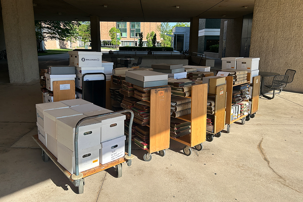A row of 9 library carts filled with boxes lined up outside.