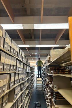 A man on a ladder in a row of archive boxes.