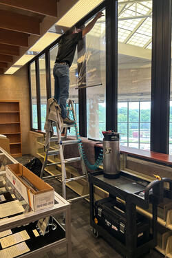 A man on a ladder installing UV film on a wall of windows.
