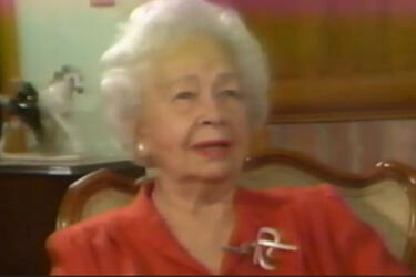 A woman in a red blouse talking to camera.
