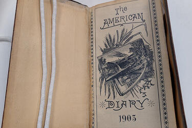 A diary opened to the cover page with the words "The American Diary 1903."