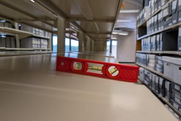 A level on an empty shelf. The level shows the shelf is sloping.
